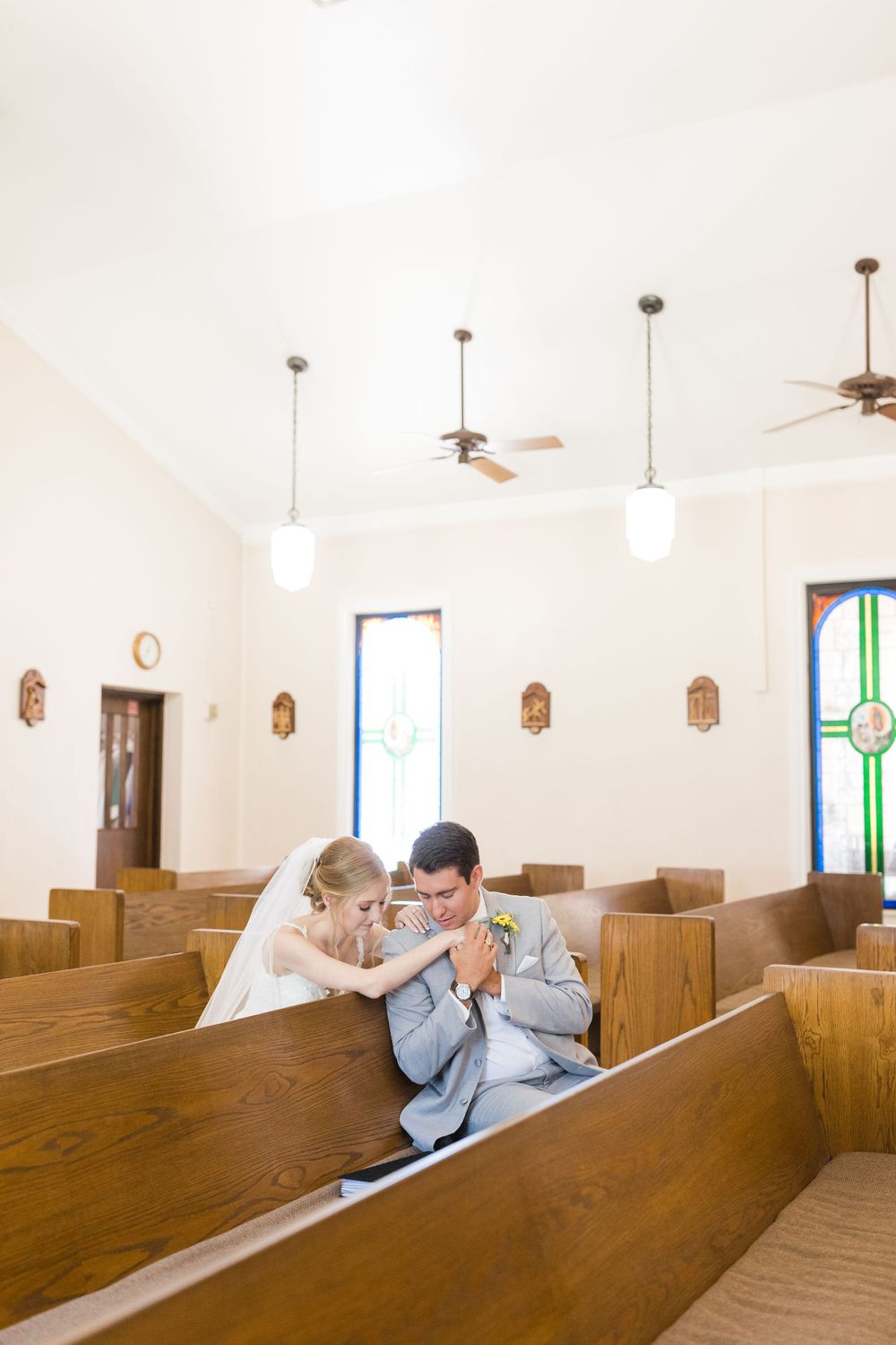 Wedding couple sharing tender moment in empty chapel with stained glass windows.