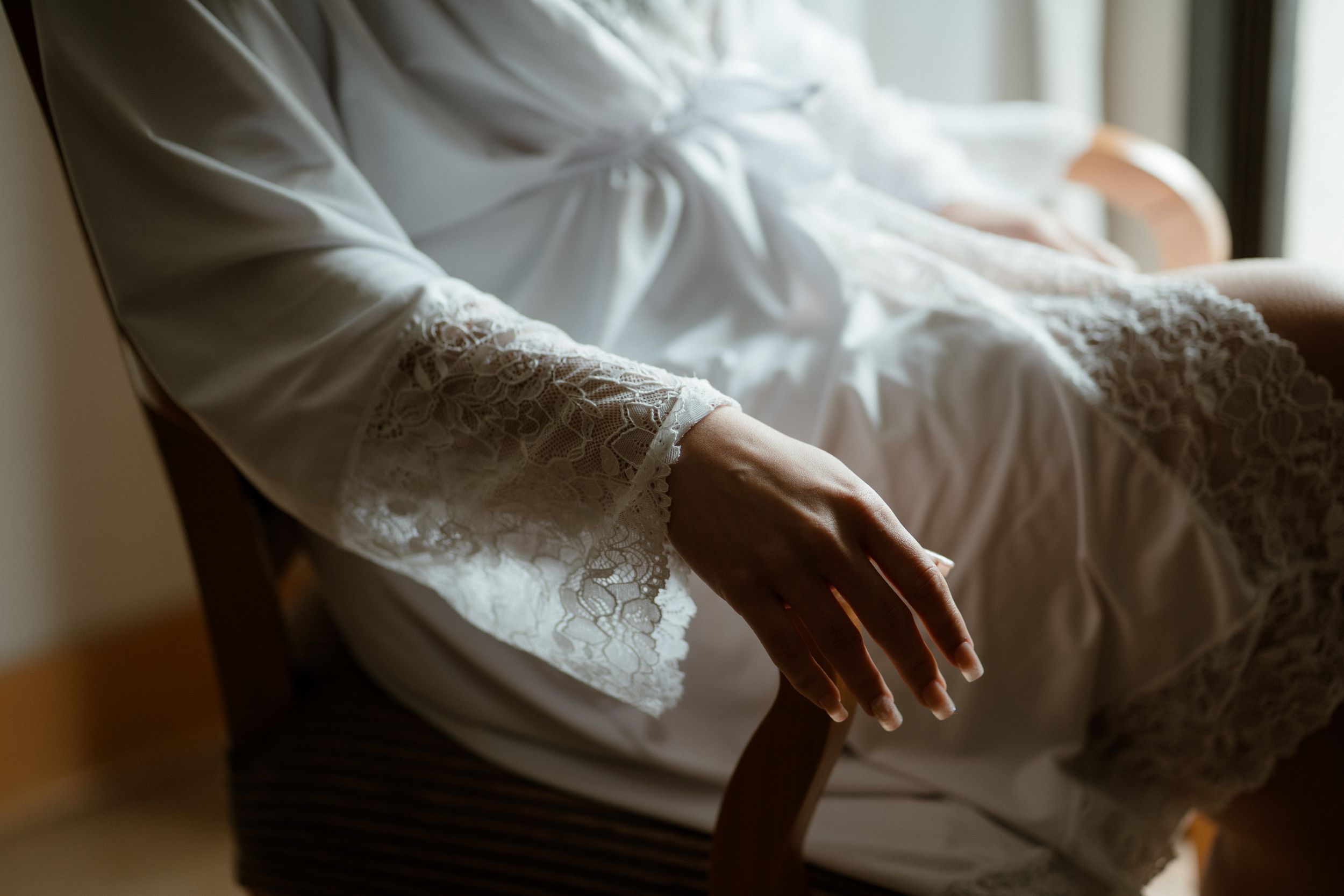 Close-up of lace detail on white wedding dress sleeve in soft window light.