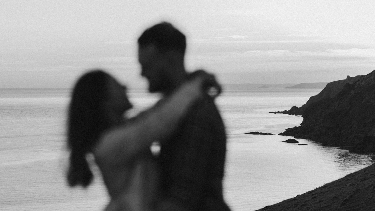 Silhouetted figures embracing against coastal sunset backdrop.