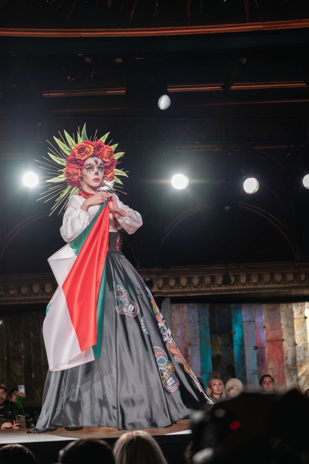 Theatrical performer on stage wearing dramatic floral headdress and flowing black and white gown during fashion show.