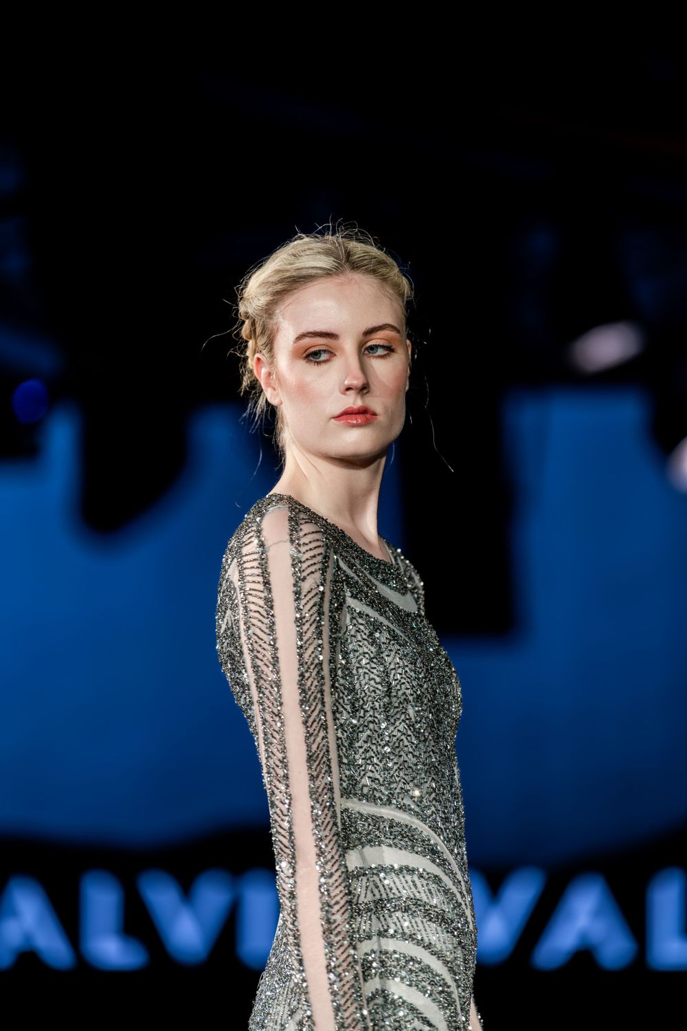 A fashion model on the catwalk wearing a shimmering silver evening gown with sheer details.