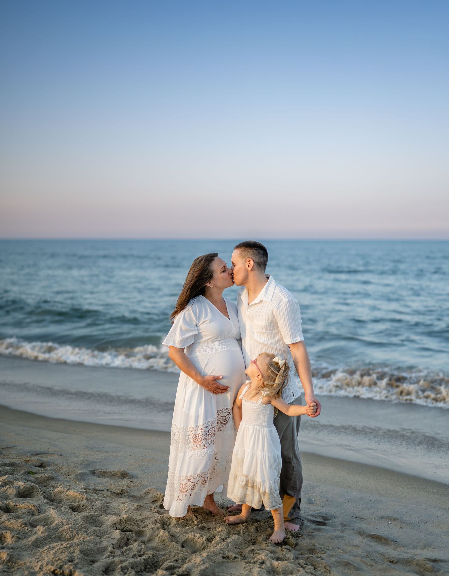 Couple sitting on beach looking at ultrasound photos together near rocky shoreline.