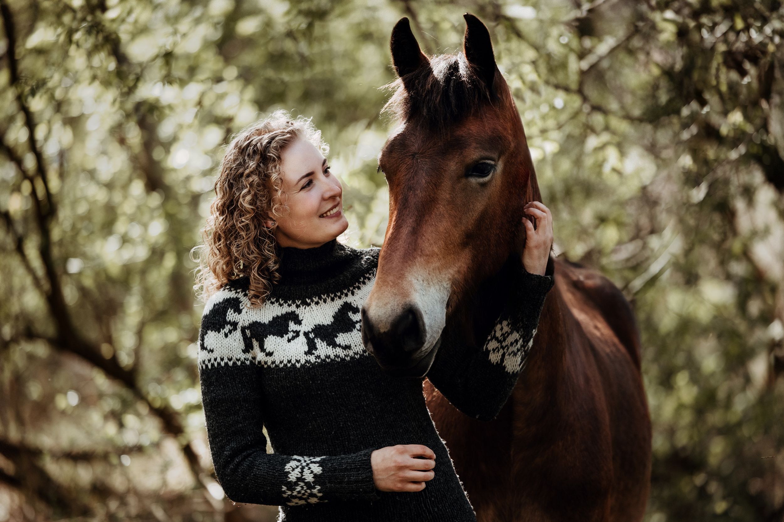 A chestnut horse and companion share a tender moment in a wooded setting.