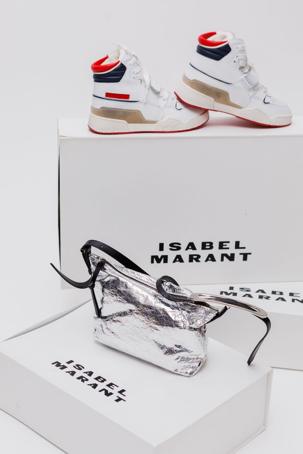 White Isabel Marant sneakers with red accents displayed alongside metallic packaging on white background.