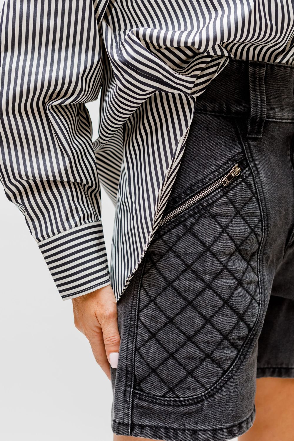 Close-up detail of black denim jeans with quilted stitching pattern and striped fabric peeking through.