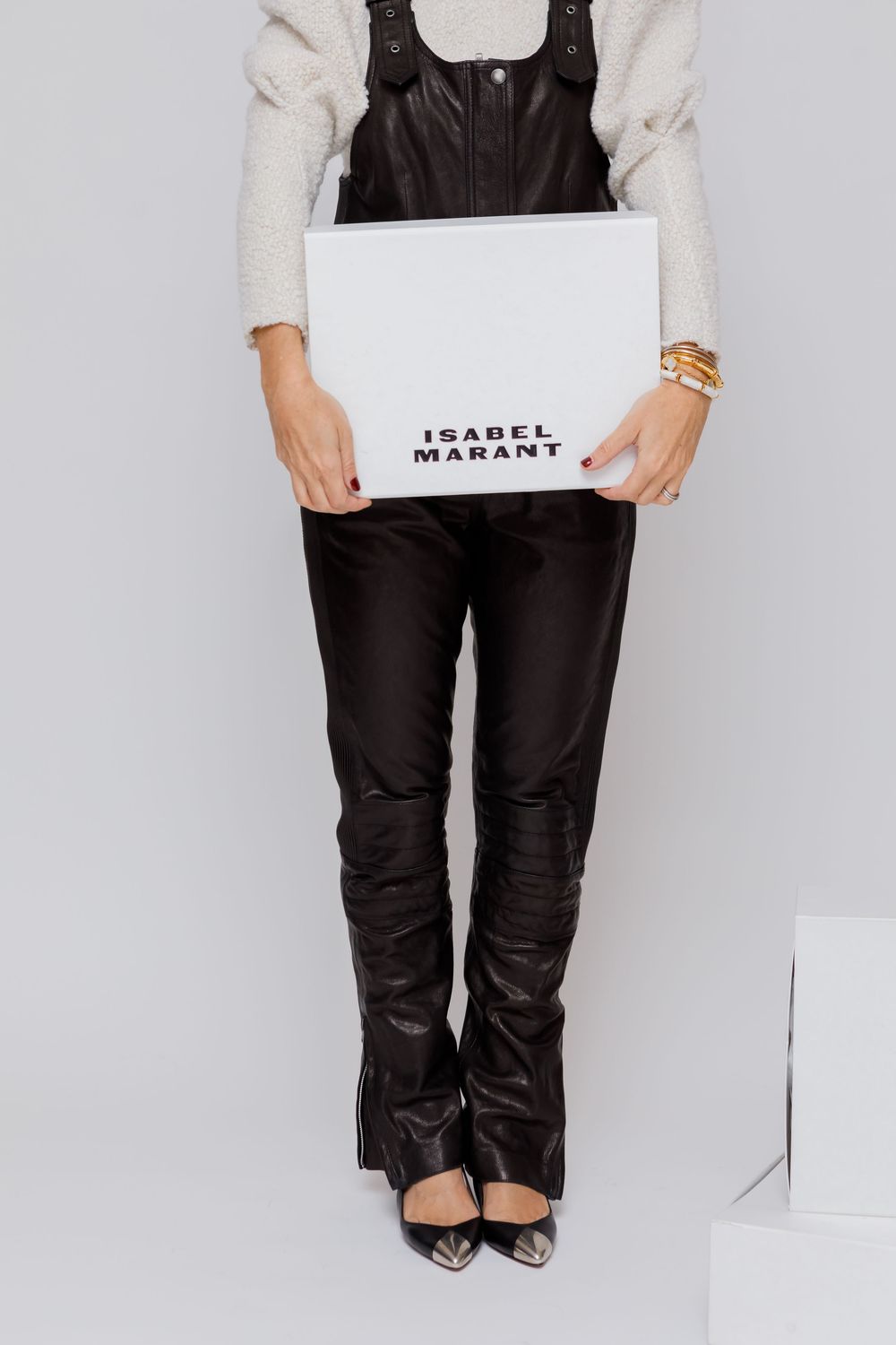 Close-up view of black leather pants and pointed heels against white background in fashion product photography.