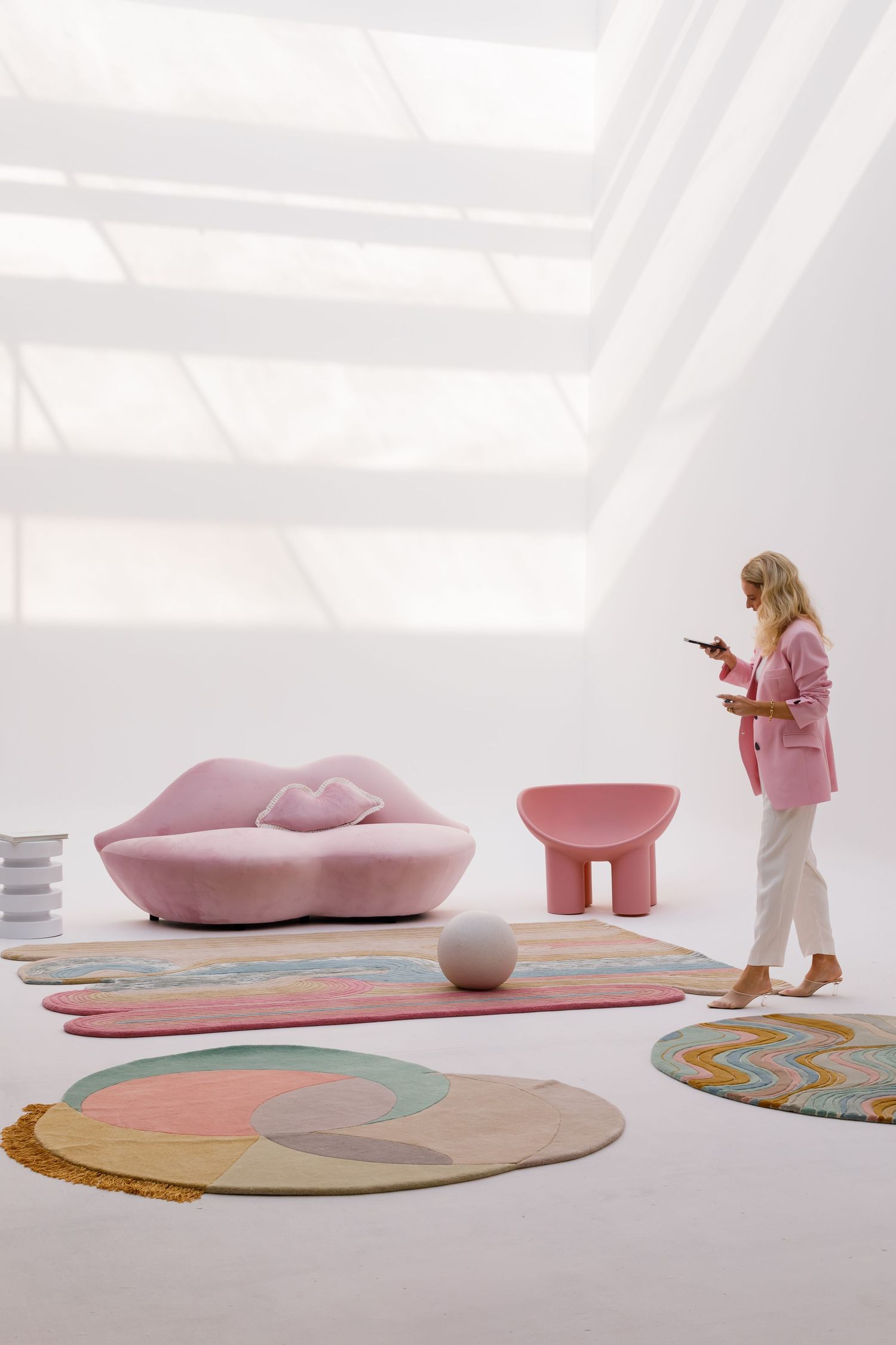Modern pink living room with sculptural sofa, round rugs and person using phone in minimalist white interior space.