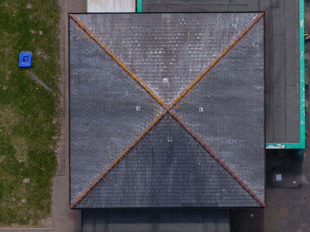 Aerial view of a gray tiled roof with a distinctive X-shaped pattern formed by copper or metal strips.