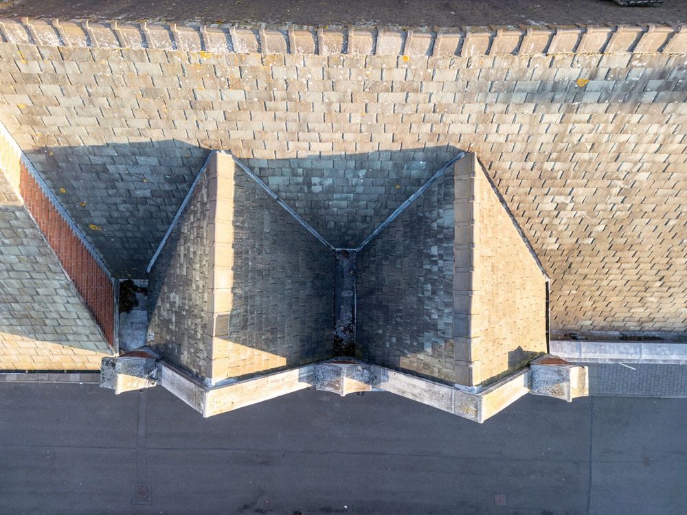 Aerial view of geometric dormers and brick shingles on a traditional residential rooftop.