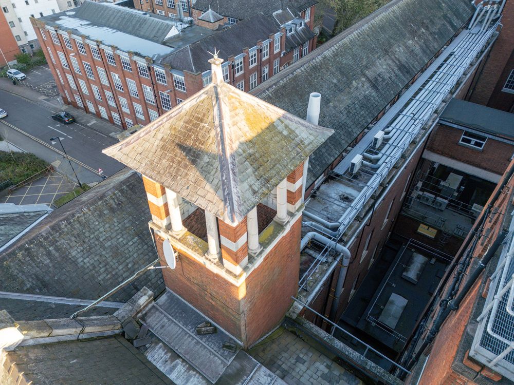 Aerial drone view of illuminated church steeples towering over red brick buildings in a historic cityscape at dusk.