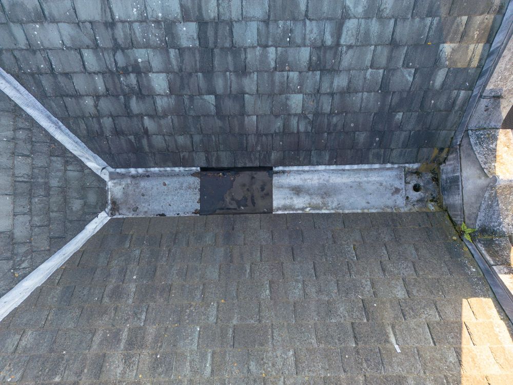 A close-up view of gray asphalt shingles on a residential rooftop showing weathered and aging texture patterns.