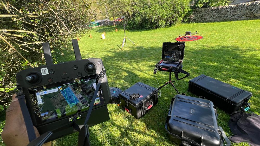 Gaming setup with monitors, laptops and equipment arranged outdoors on a lawn on a sunny day.