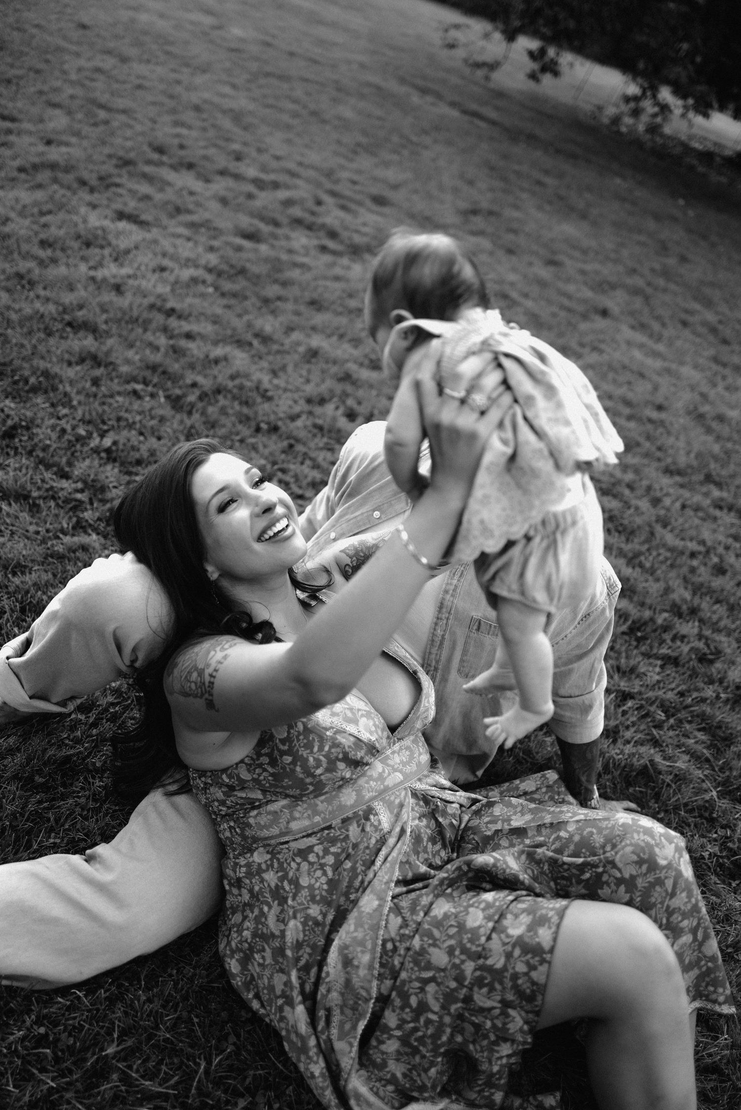 A joyful moment captured in black and white as someone lies in the grass wearing a floral dress.