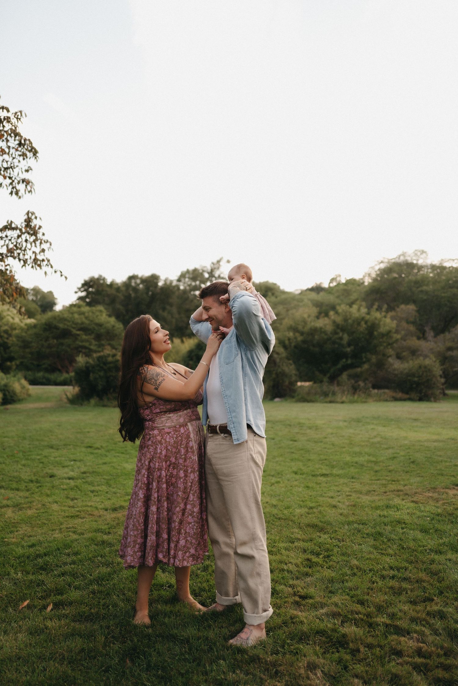A romantic couple shares tender moments in a grassy field during a sunset photo session.