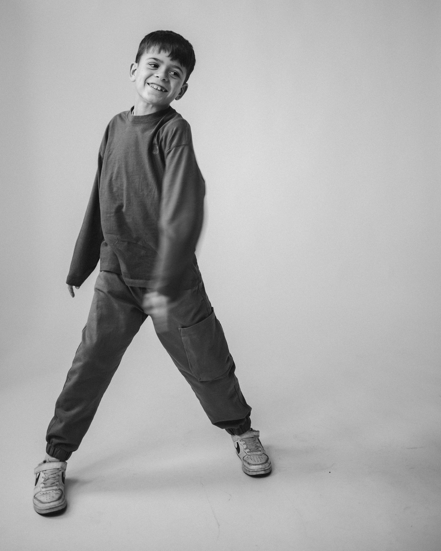 A black and white photo series showing a child in casual wear making playful dance-like poses against a plain backdrop.