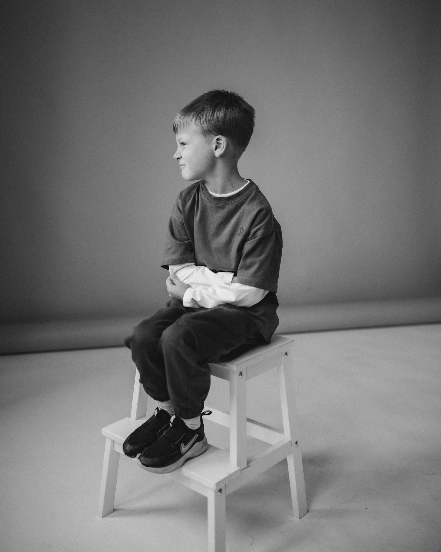 A sequence of black and white photos showing a child sitting on a white stool in various contemplative poses.