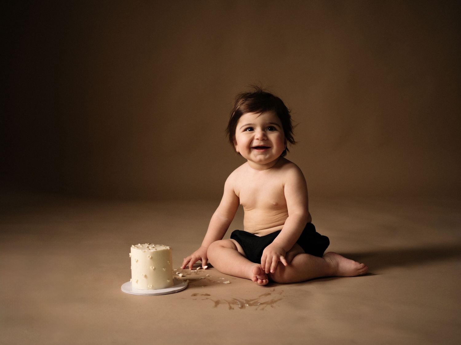 Studio portrait with small cake and brown backdrop in warm lighting.