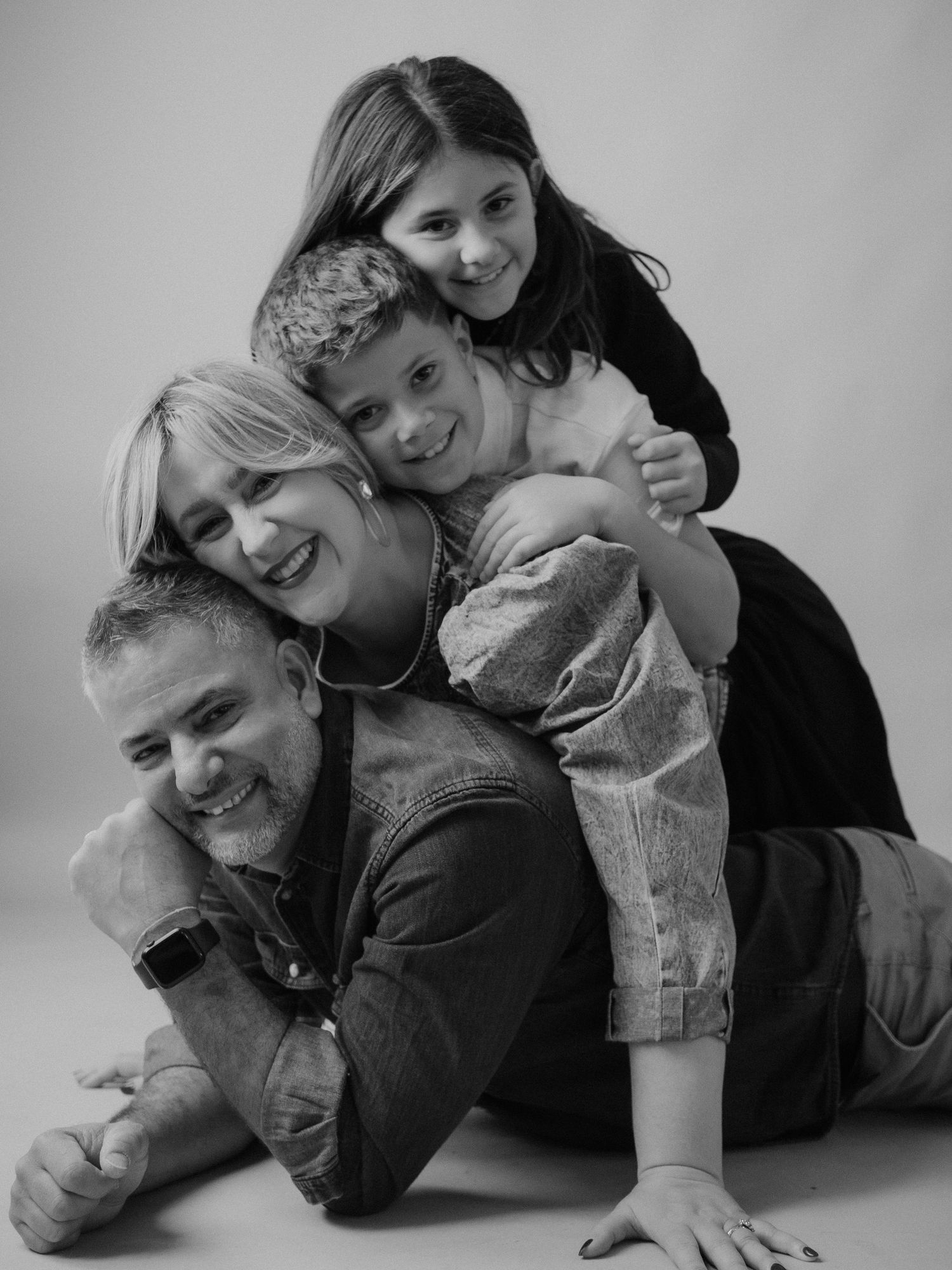 Black and white portrait of a family playfully piled on top of each other on the floor in a casual studio setting.