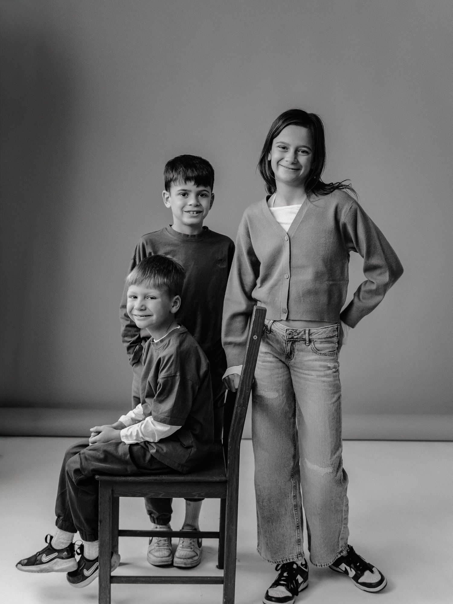 A series of black and white photos showing a young child sitting on a chair next to someone standing in casual attire.
