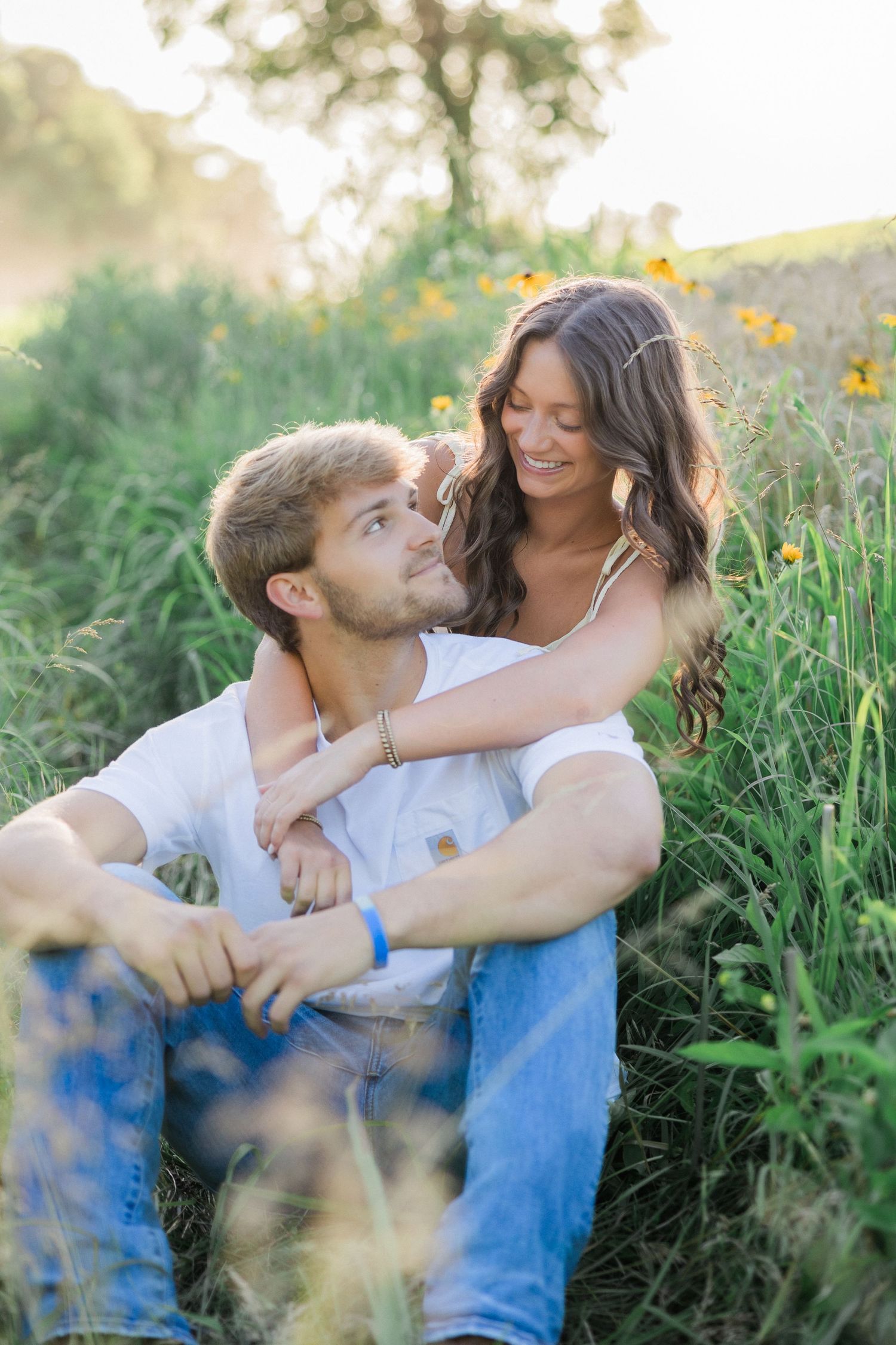 A couple sits together in a field of wildflowers during golden hour.