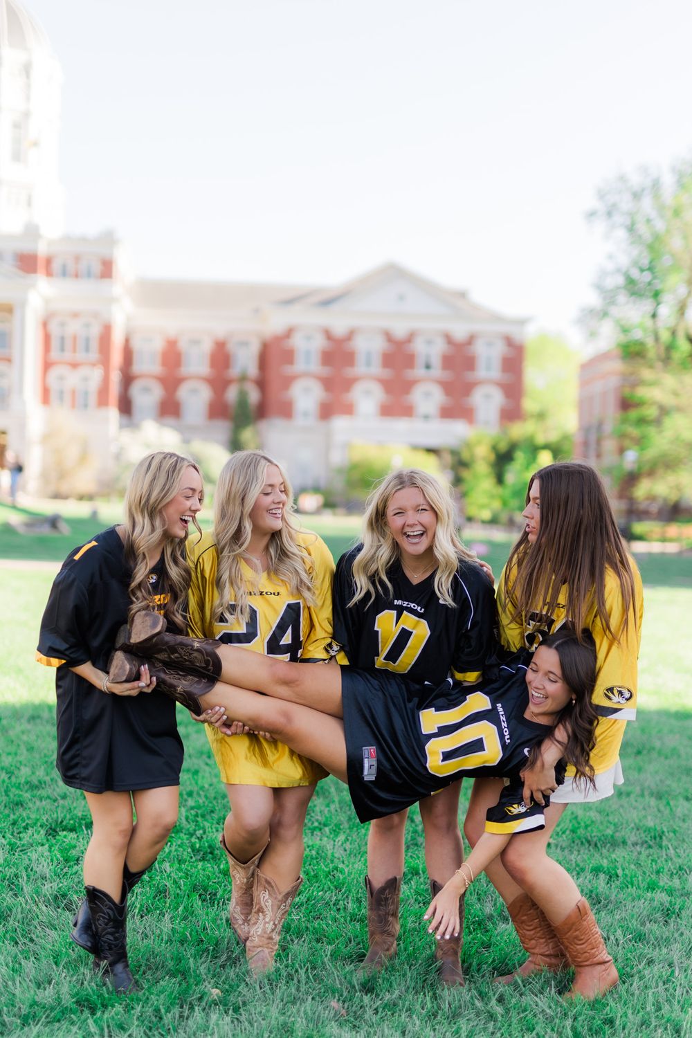 Friends in yellow and black sports jerseys laugh together on university lawn.