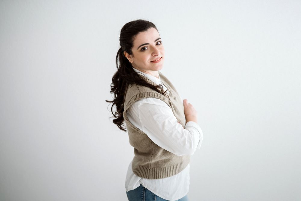 Photographer in white sweater posing with camera in studio setting.