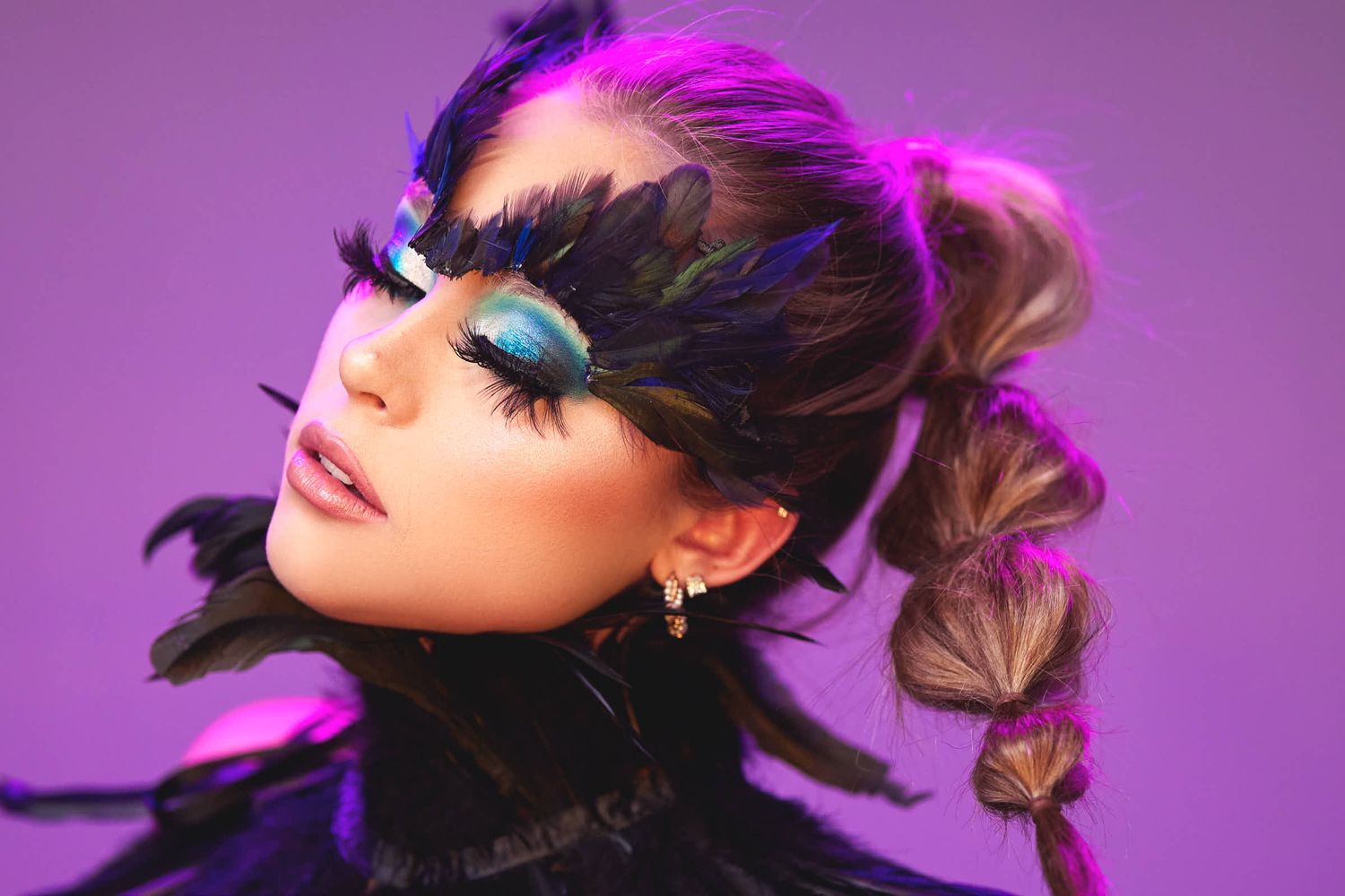 Creative beauty portrait with dramatic makeup, feathers and bubble ponytail against purple background.