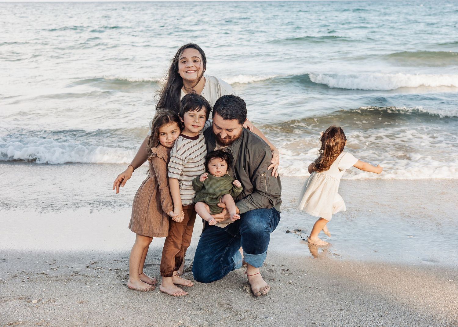 Family enjoying a sunny day together at the beach with waves crashing on the shore in the background.