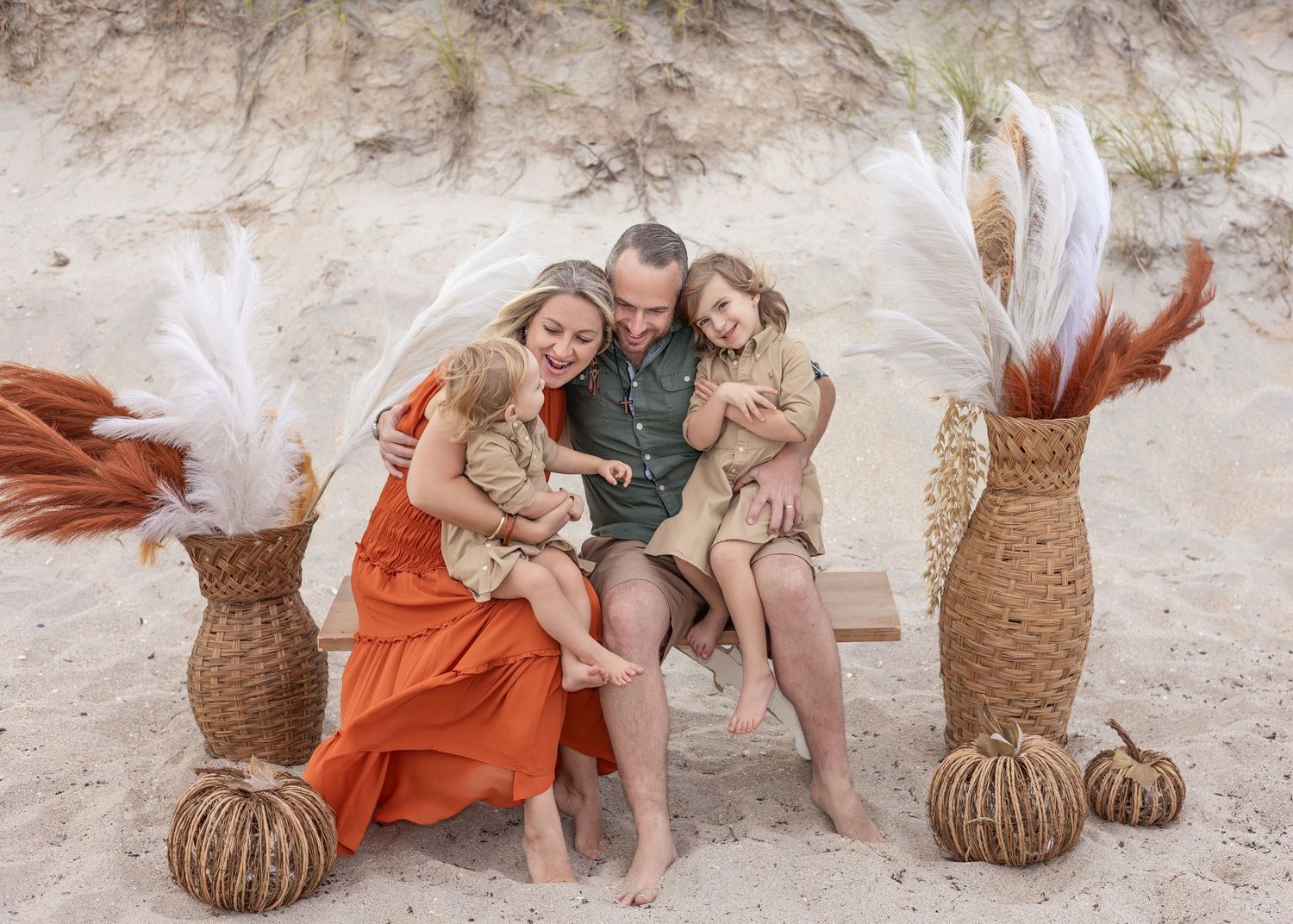 Lifestyle photo session on sandy beach with woven baskets and flowing rust-colored dress creates dreamy coastal aesthetic.