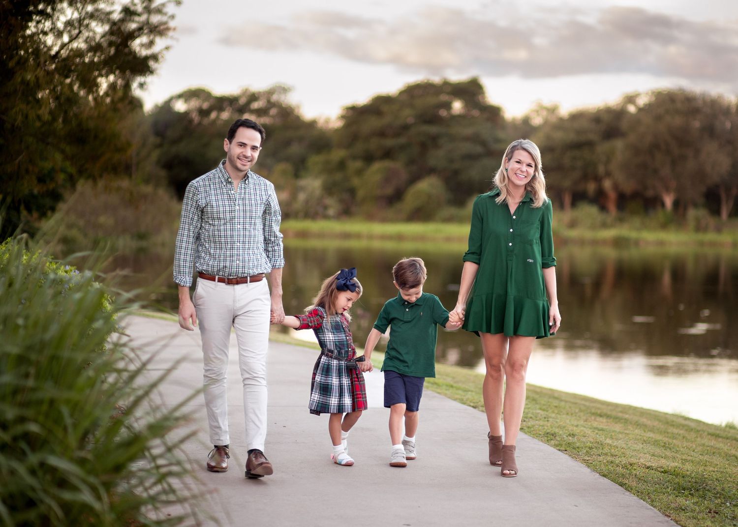 A family takes an evening stroll along a scenic lakeside path surrounded by lush greenery at sunset.