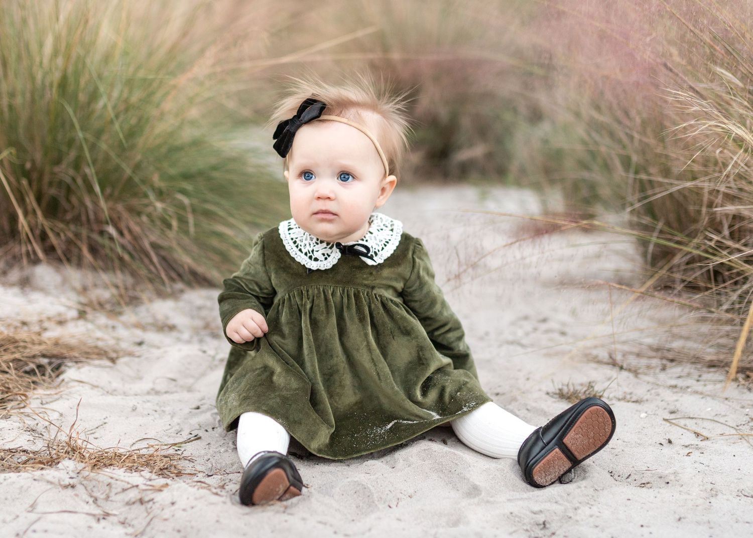 A toddler in a green sweater plays in the sand at the beach while crawling and exploring.