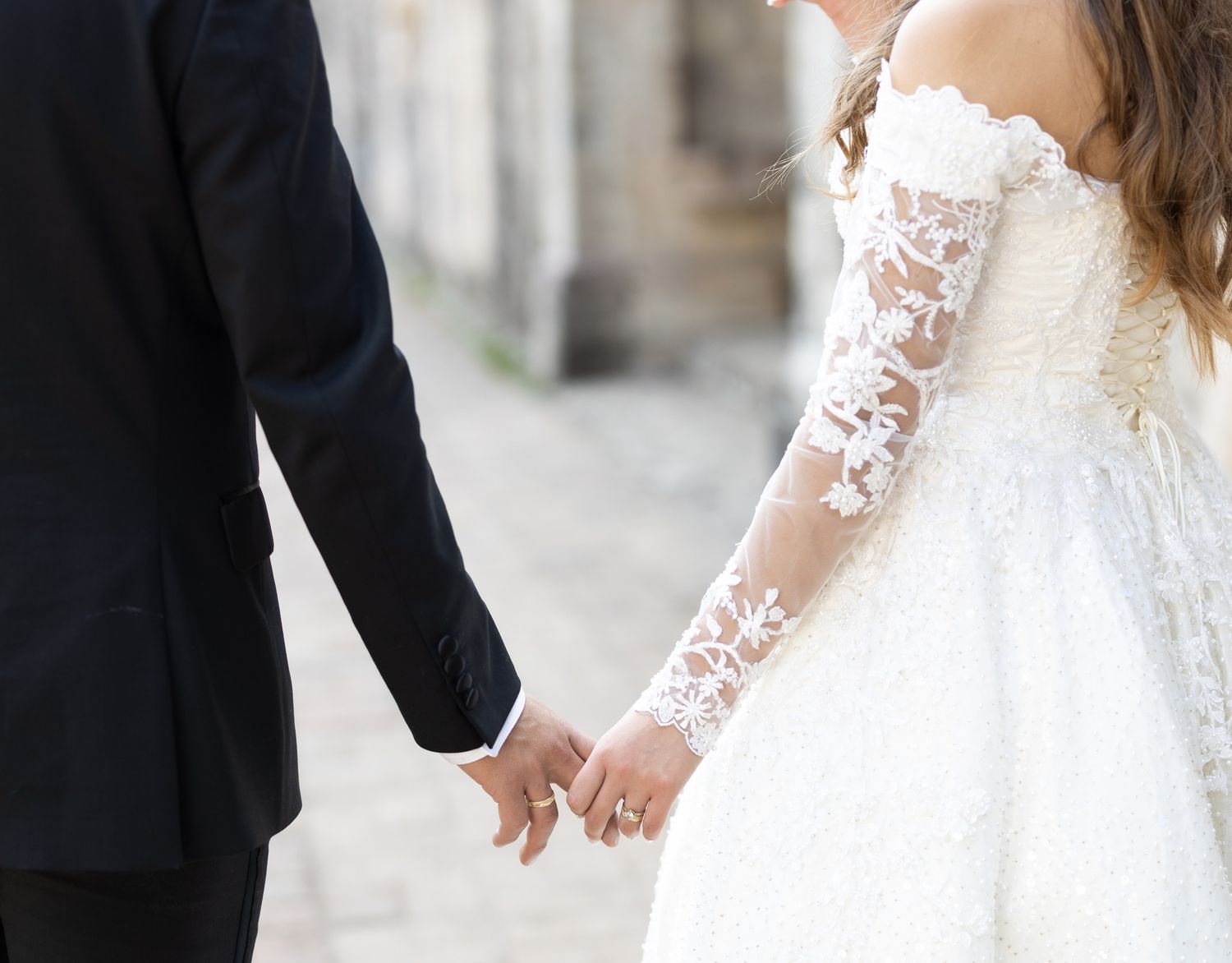 Close-up of bride and groom holding hands, showcasing delicate lace sleeve details.