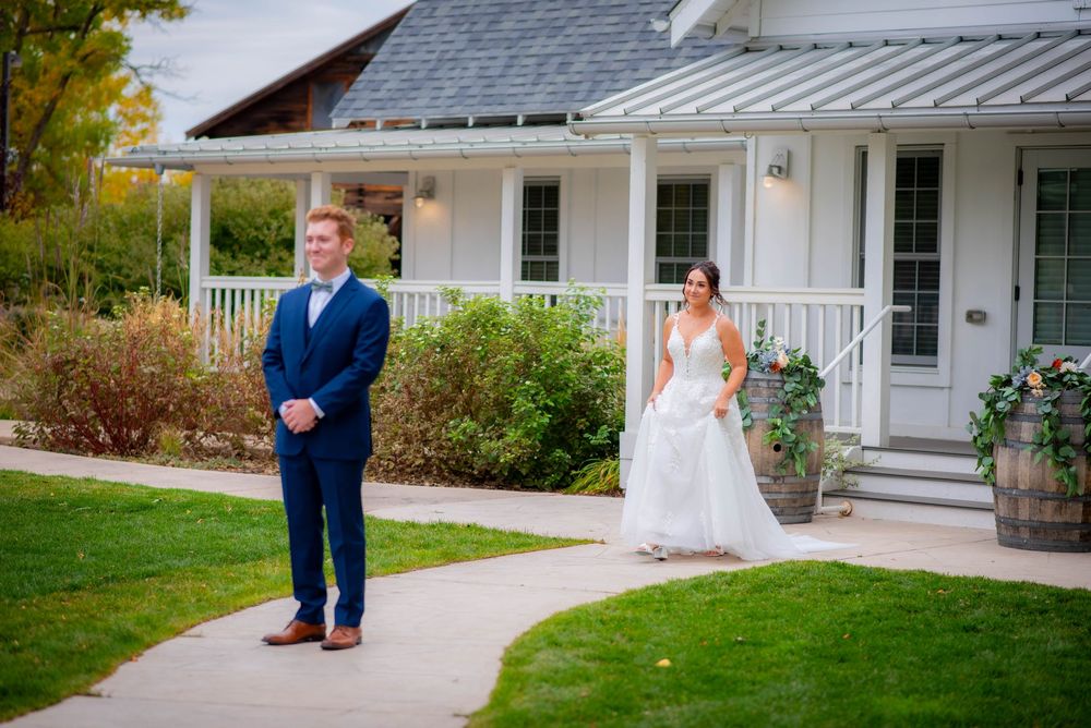 First look moment between wedding couple outside a charming white farmhouse with wraparound porch.