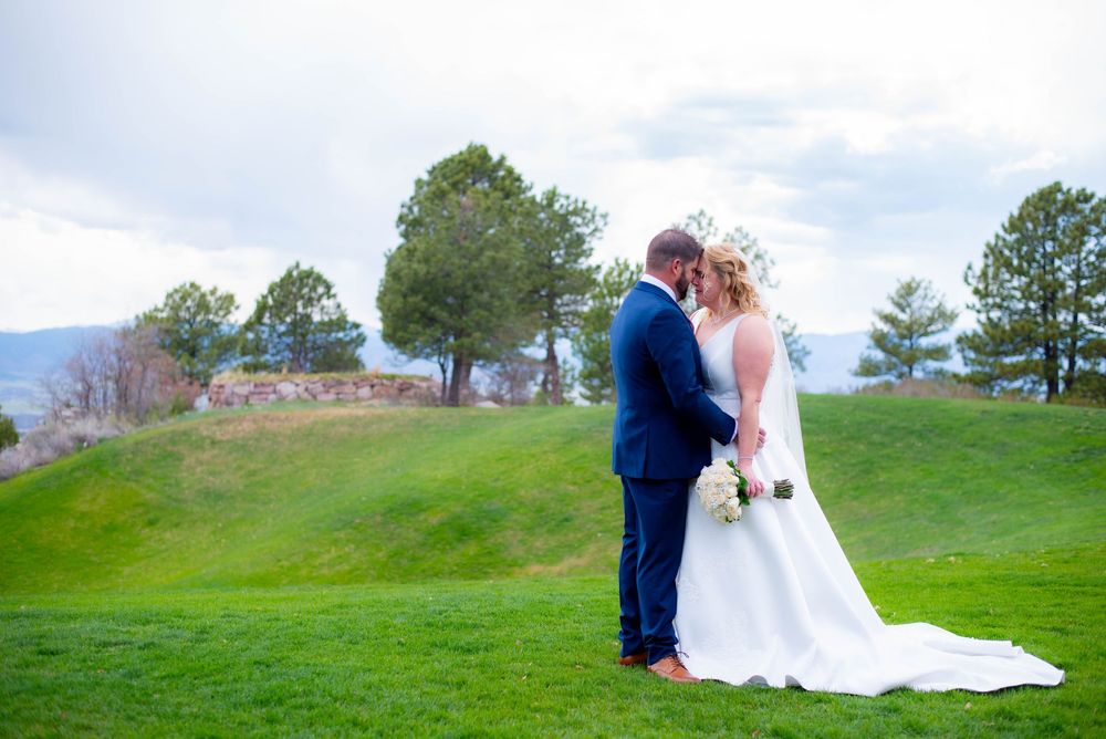 Wedding couple embraces on hilltop with mountain views and green grass.