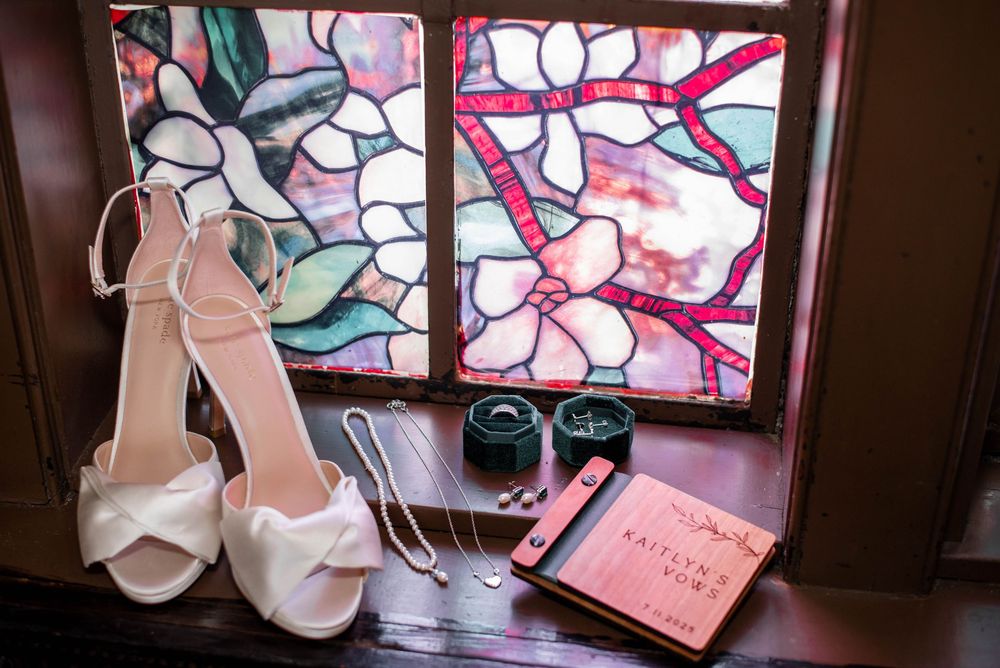 Wedding details including white heels, rings, and stained glass window with pink floral design.