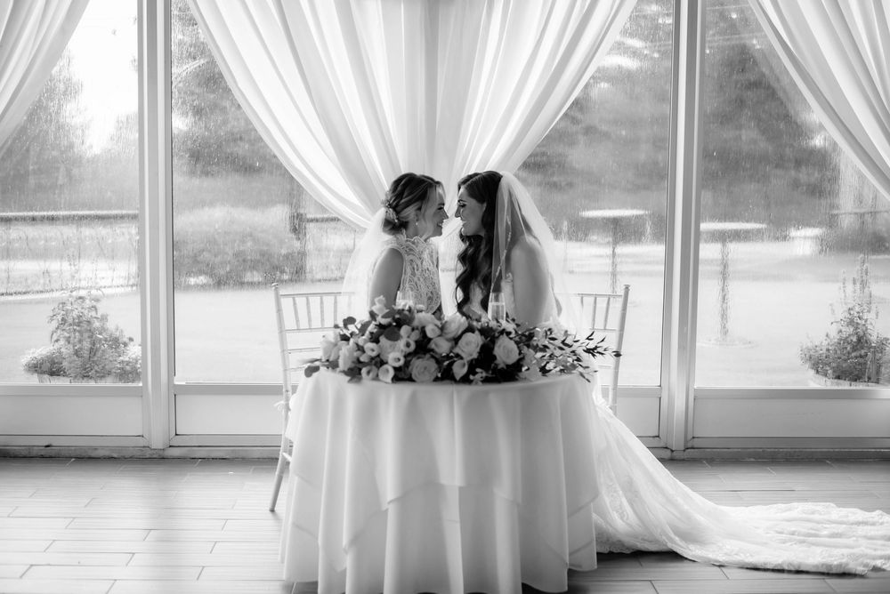 Two brides share an intimate moment at their wedding reception table adorned with elegant floral arrangements.