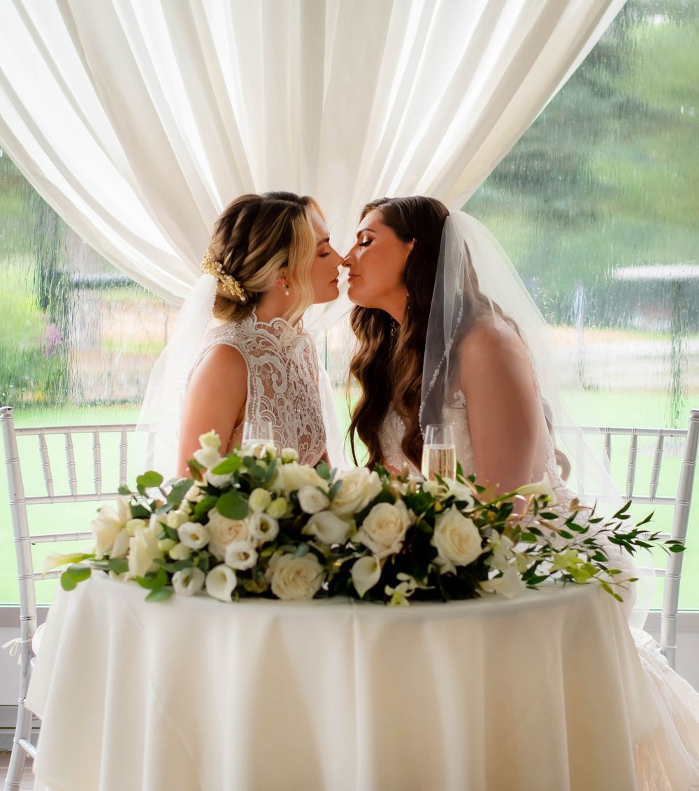 A romantic moment between newlyweds at their reception table decorated with white roses and greenery.