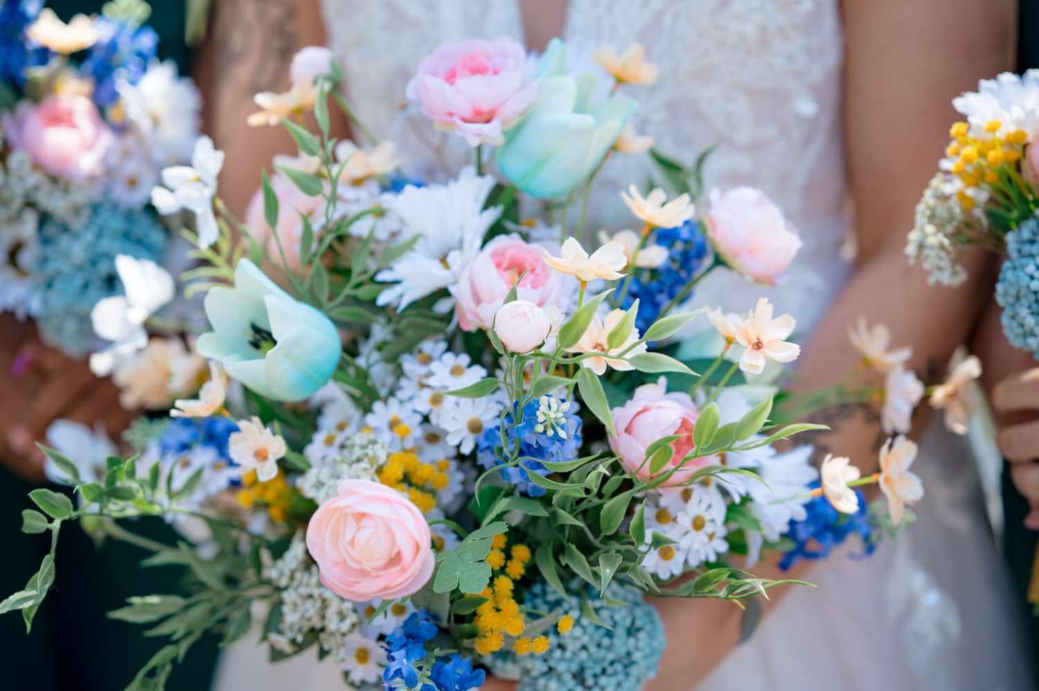 A beautiful wedding bouquet with pink roses, blue delphiniums, and mixed pastel flowers arranged naturally.