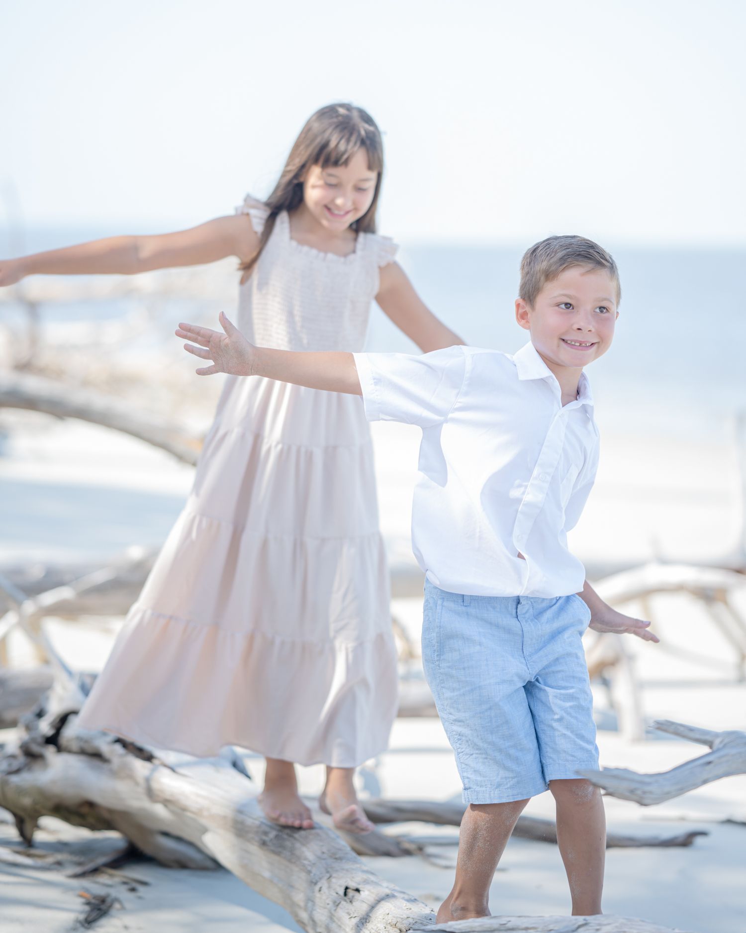 Children playing and posing on driftwood at sunny beach in light summer clothing.