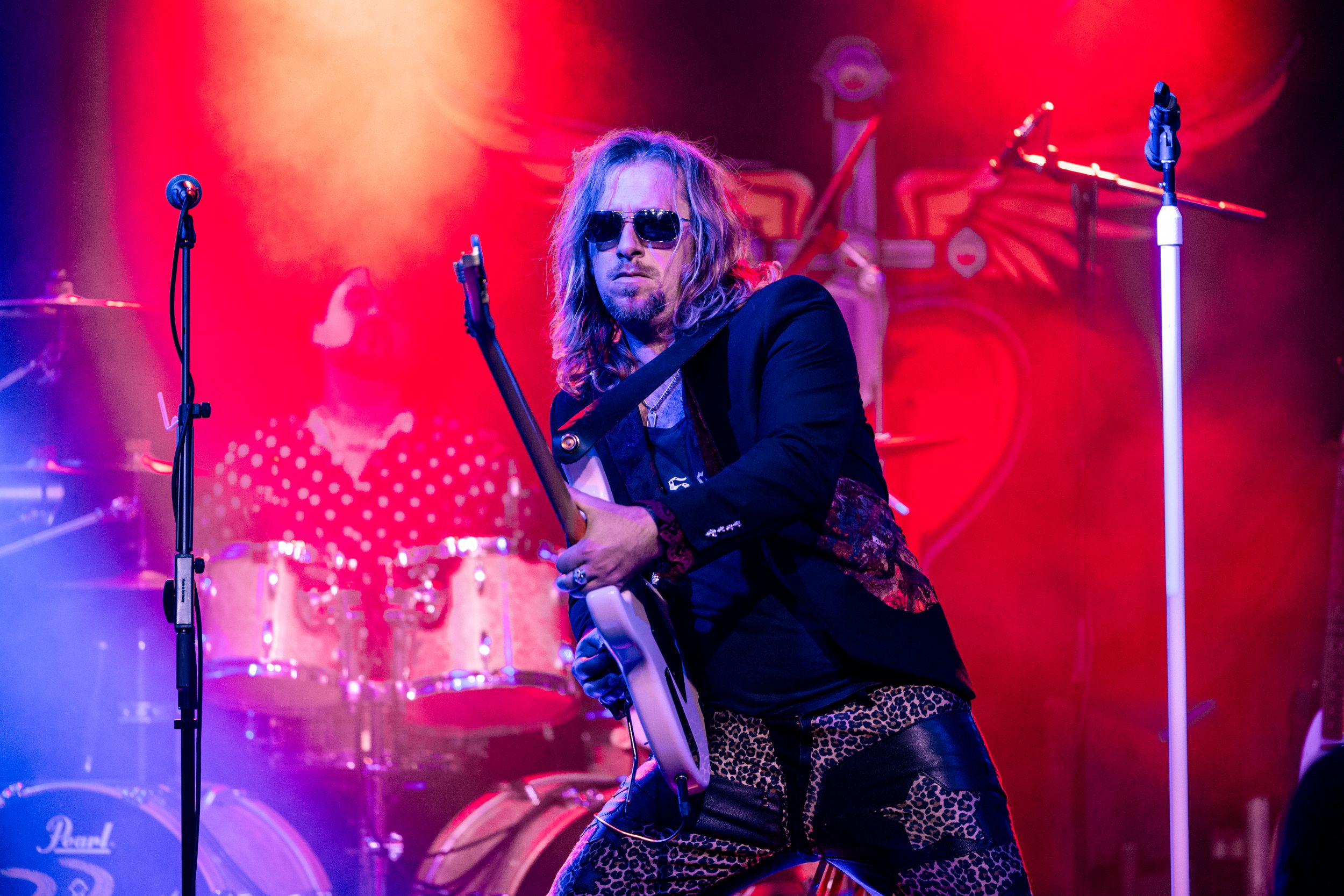 Rock musician performing on stage with red lighting effects.