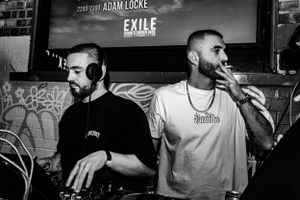 Two DJs performing at nightclub event with text projection in background.