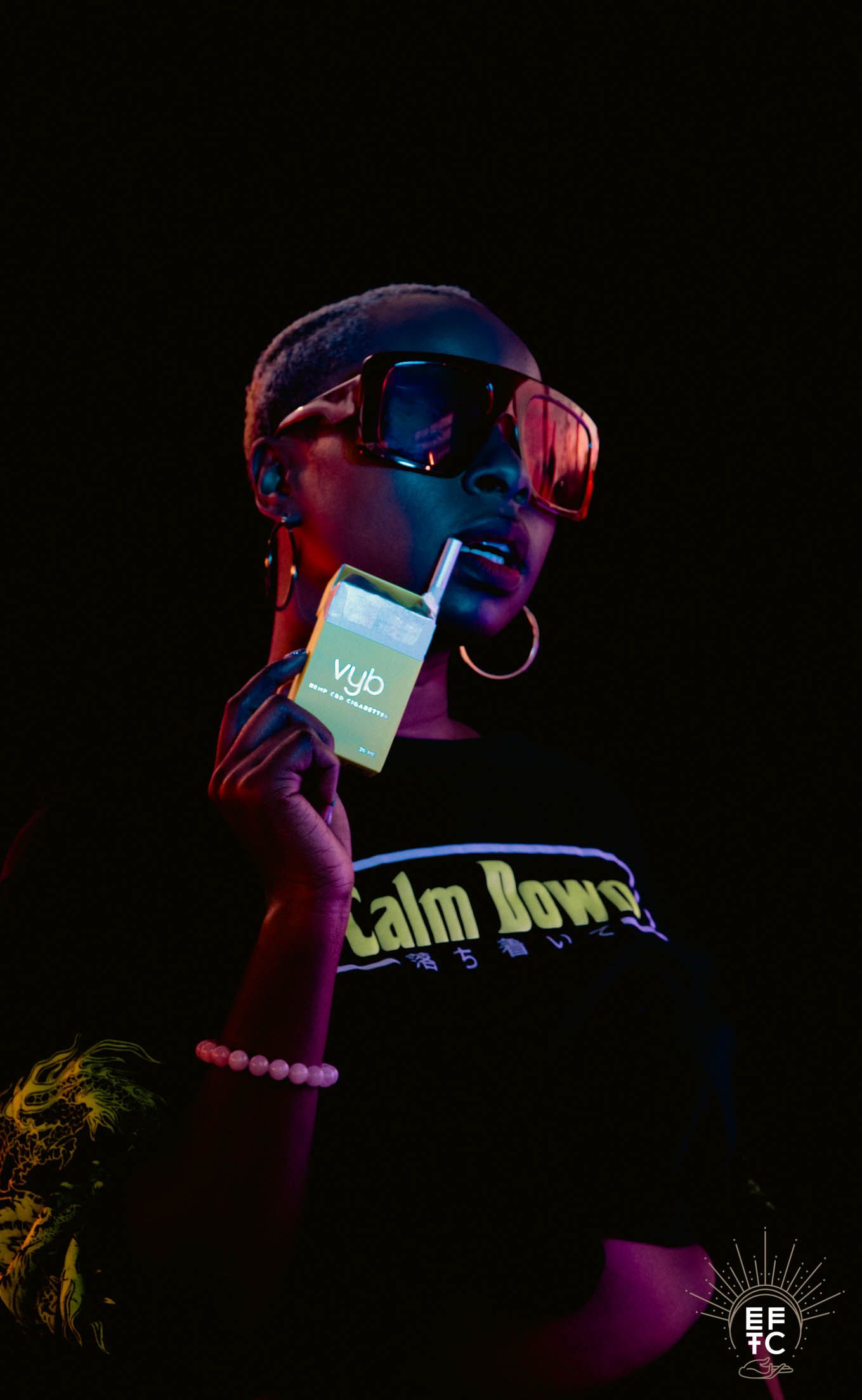 Concert performer illuminated by vibrant pink and blue lighting wearing sunglasses in dark atmospheric stage setting.