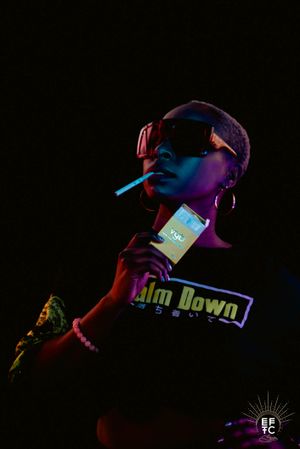 Dark artistic photo with neon lighting shows person with a cigarette wearing sunglasses casual attire in dramatic purple and red tones.