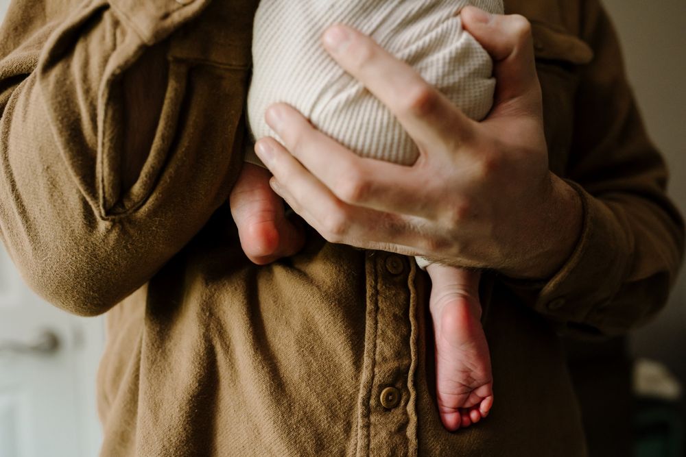 Dad embraces newborn baby and baby's feet dangle down