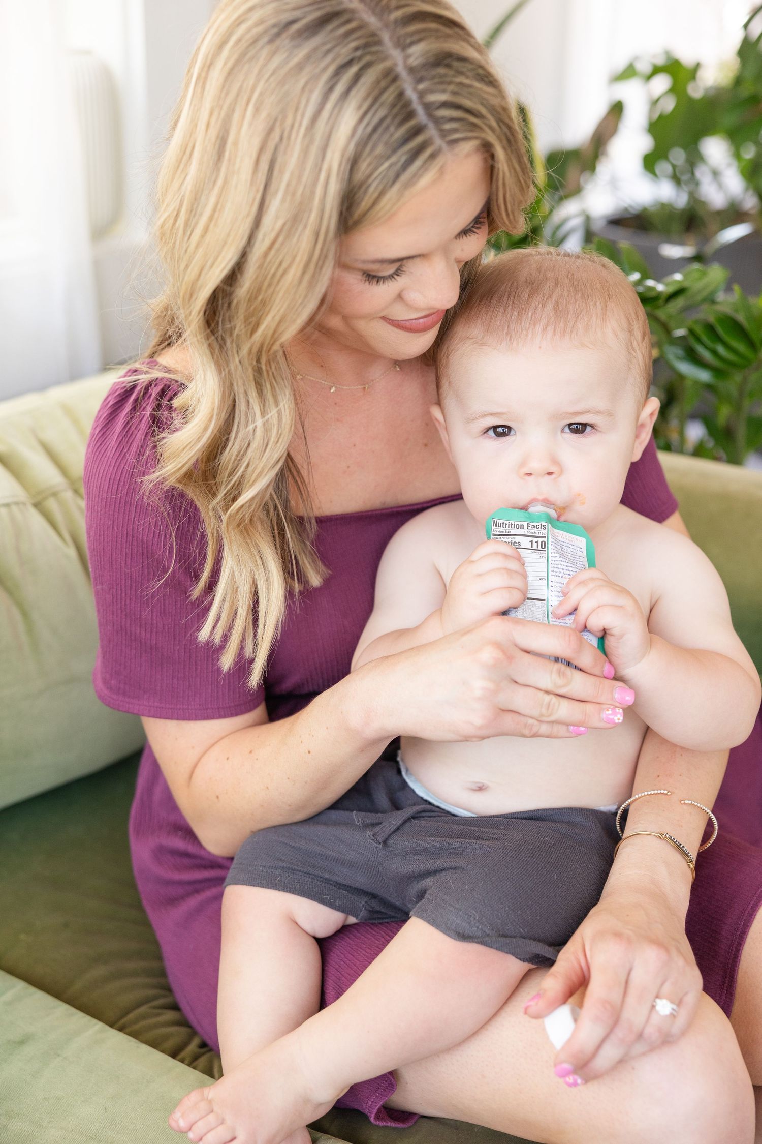 A tender moment on a green couch as an infant drinks from a small container.