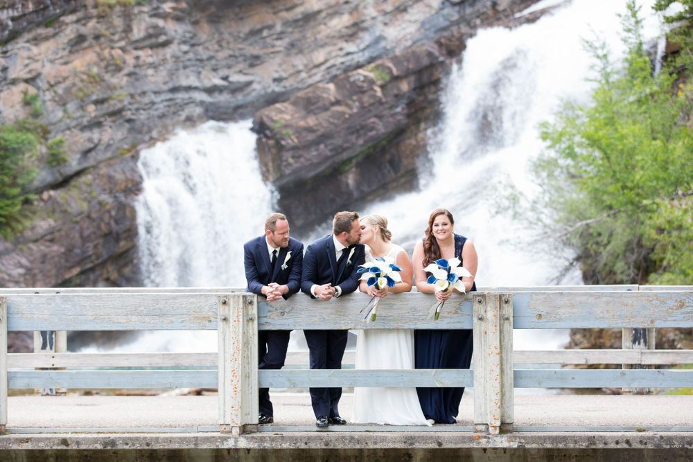 Wedding couple poses on bridge with majestic waterfall in background.