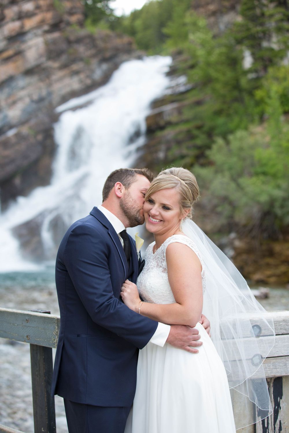 A romantic wedding photo session in front of a cascading waterfall with mountains in the background.