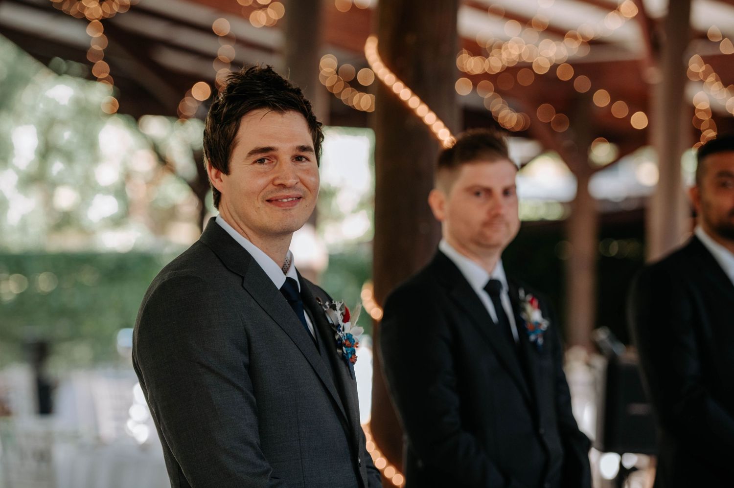 Wedding party members standing at altar during outdoor ceremony with string lights.