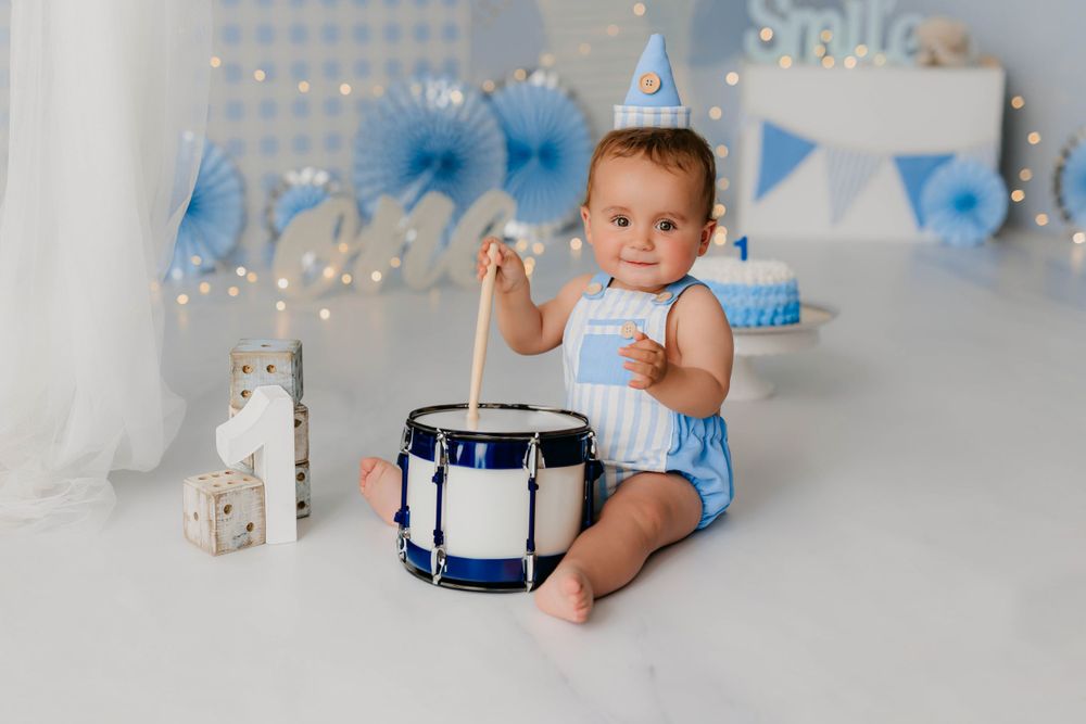 Foto del primer añito de un niño tocando un tambor y peto en tonos azules en su sesión en estudio.