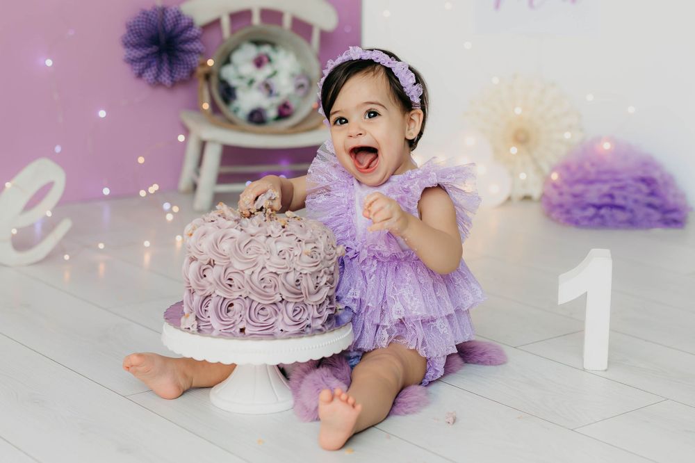 Fotografía del primer añito de una niña con tarta y con decoración en tonos morados en su sesión de estudio.